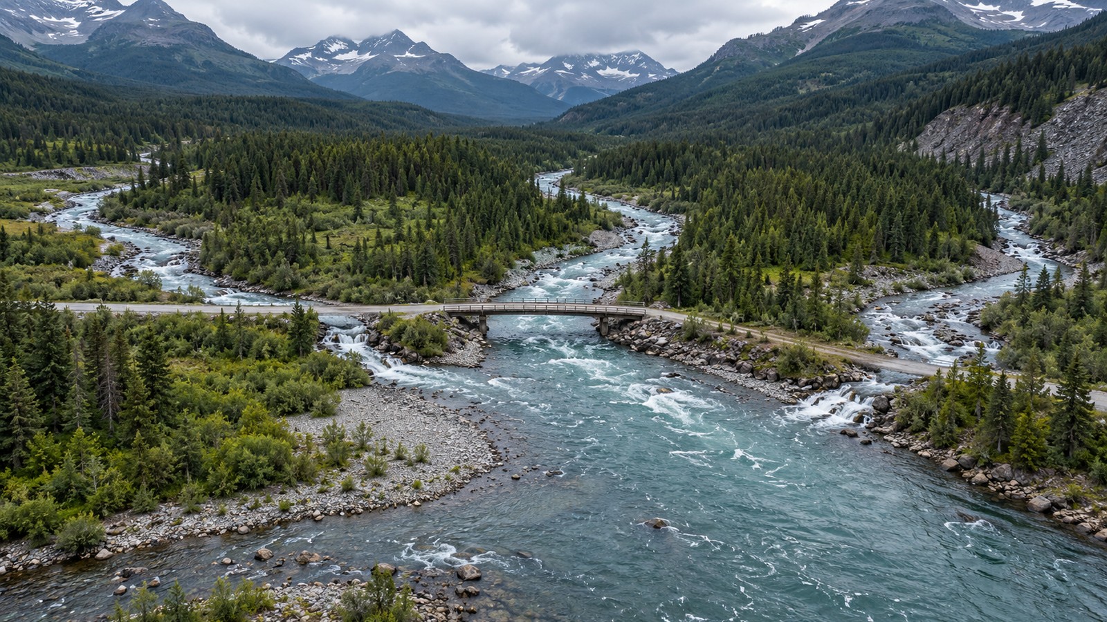An aerial view of a braided river with a bridge in mountain terrain.