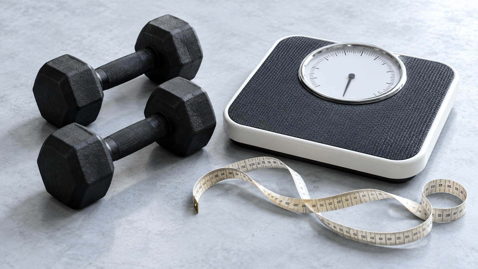 Two dumbbells resting on a bathroom scale beside a measuring tape.